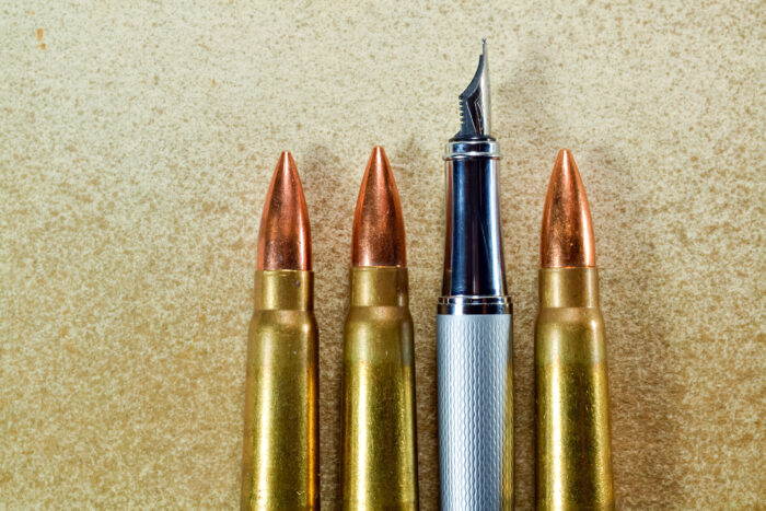 Pen and three bullets arranged verticaly on vintage background. Symbolize the confrontation between the power of the written word and the power of weapons and politics.