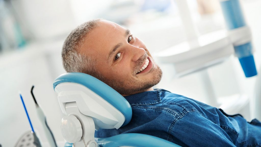 Homrbre sonriendo en una consulta de odontología